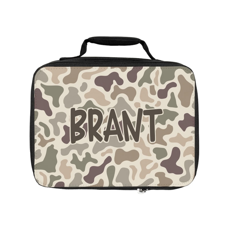 K&ouml;nnte beinhalten: Eine rechteckige Lunchtasche mit schwarzem Griff und schwarzem Rand, die ein Tarnmuster in Beige-, Sand-, Olivgr&uuml;n- und Dunkelbraunt&ouml;nen aufweist. Der Name BRANT ist in gro&szlig;en, dunkelbraunen, serifenlosen Gro&szlig;buchstaben in der Mitte aufgedruckt.