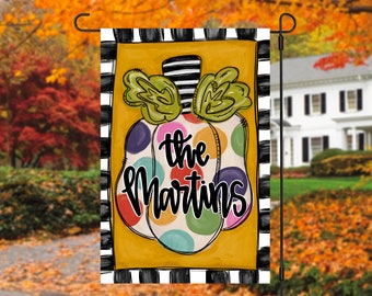 May include: A colorful, polka-dotted pumpkin with a black and white striped stem. The text "the Martins" is written in black on the pumpkin. The pumpkin is on a yellow background with black and white stripes around the edges.