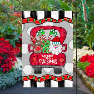 May include: A red truck with a white "Merry Christmas" banner on the back. Santa Claus, an elf, and a reindeer are riding in the truck bed. The truck is on a gray background with white polka dots and black and white stripes.