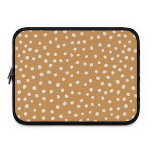 May include: A mustard-colored laptop sleeve with a repeating pattern of white polka dots. The sleeve has a black zipper and black trim. The design is simple and modern, suitable for protecting a laptop or tablet.