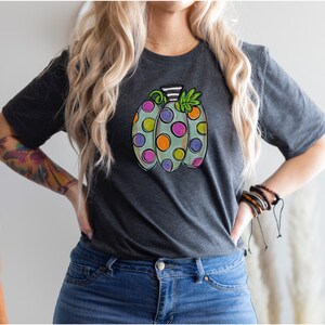 K&ouml;nnte beinhalten: Dunkelgraues T-Shirt mit einem bunten K&uuml;rbisdesign. Der K&uuml;rbis ist hellgr&uuml;n mit gro&szlig;en, bunten Tupfen in Lila, Orange und Gelb. Der Stiel ist schwarz-wei&szlig; gestreift. Ein lustiges und festliches, herbstliches Grafik-T-Shirt.