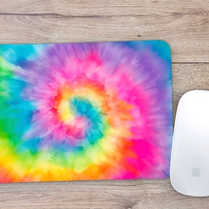 May include: A colorful tie-dye mouse pad with a swirling pattern in shades of pink, blue, green, and yellow. The mouse pad is on a wooden surface.
