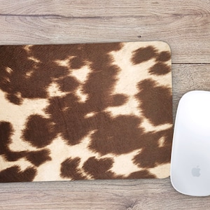 May include: A brown and white cowhide patterned mouse pad. The mouse pad is rectangular and has a smooth surface.