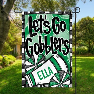 May include: A green and black garden flag with the text "Let's Go Gobblers" and a personalized name "Ella". The flag features a green and white cheerleader pom-pom.