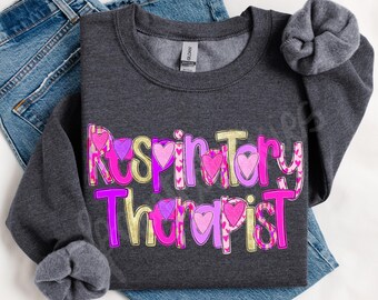May include: A dark gray sweatshirt with the text "Respiratory Therapist" in pink, purple, and gold letters with hearts. The letters are outlined in white.