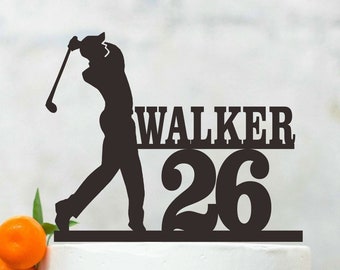 Peut inclure: Un gâteau blanc avec une silhouette noire d'un golfeur tenant un club de golf. Le dessus du gâteau comprend également le nom "WALKER" et le numéro "26".