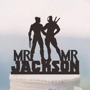 May include: Black silhouette cake topper featuring two figures, one with claws and the other with swords, standing back to back. The text "MR JACKSON MR" is below the figures.