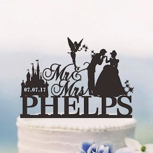 Puede incluir: Topper de pastel en silueta negra con una pareja besándose, Campanilla, un castillo y el texto "Mr. & Mrs. Phelps 07.07.17".