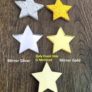 Op de afbeelding: Vijf verschillende stervormige decoraties in verschillende afwerkingen. Van links naar rechts: glitter zilver, spiegel zilver, hout, spiegel goud en glitter goud. De tekst "Only Front Side Is Mirrored" staat onder de sterren.