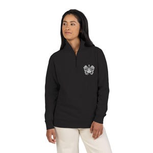 May include: Black long-sleeve pullover with a quarter-zip neckline. A white butterfly design is on the upper left chest. The model is wearing off-white pants. The pullover is made of a soft material.
