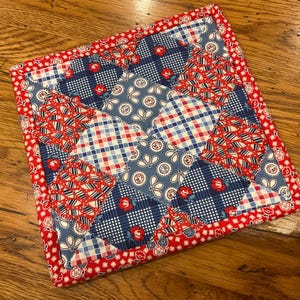 May include: A square patchwork quilt with a red border. The quilt features a mix of red, white, and blue fabrics in various patterns, including gingham, floral, and paisley designs. The quilt is approximately 10 inches square.