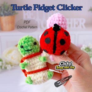 Op de afbeelding: Gehaakte schildpad- en lieveheersbeestje fidget clickers met klikhaarclips. De schildpad is groen en crème met een oranje rand. Het lieveheersbeestje is rood met zwarte stippen. De tekst "Turtle Fidget Clicker" is inbegrepen.