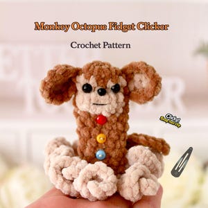 May include: A handmade crochet Monkey Octopue Fidget Clicker in shades of brown and beige. The toy features a monkey face with black eyes and colorful buttons. The text "Monkey Octopue Fidget Clicker Crochet Pattern" is displayed above the toy.