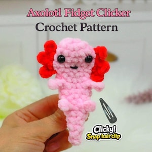 May include: A pink crocheted axolotl fidget clicker with red gills and black eyes. The text "Axolotl Fidget Clicker Crochet Pattern" is at the top. A black snap hair clip is next to the axolotl, with the text "Clicky! Snap hairclip".