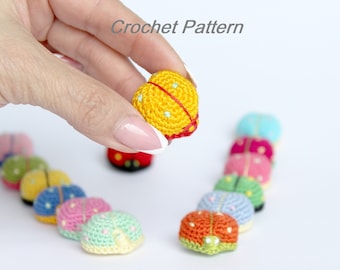 May include: A line of colorful crocheted ladybugs, with one ladybug held in a hand. The ladybug in the hand is yellow with green spots and red trim. The other ladybugs are various colors, including red, pink, green, and blue.