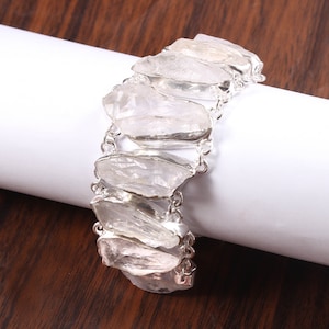 Pode incluir: Um bracelete de corrente de prata com pedras de cristal de quartzo transparente. As pedras são facetadas e têm um aspeto natural e bruto.