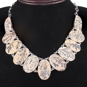 May include: A silver necklace with a pattern of oval-shaped stones. The stones are a light brown color with a dark brown dendritic pattern.