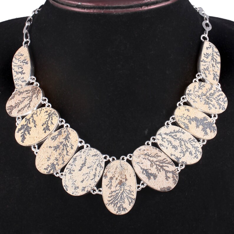 May include: A silver necklace with a pattern of oval-shaped stones. The stones are a light brown color with a dark brown dendritic pattern.