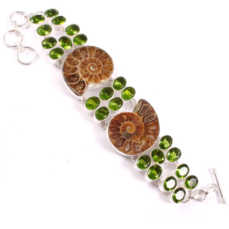 May include: A silver bracelet with two brown ammonite fossils and green peridot gemstones.