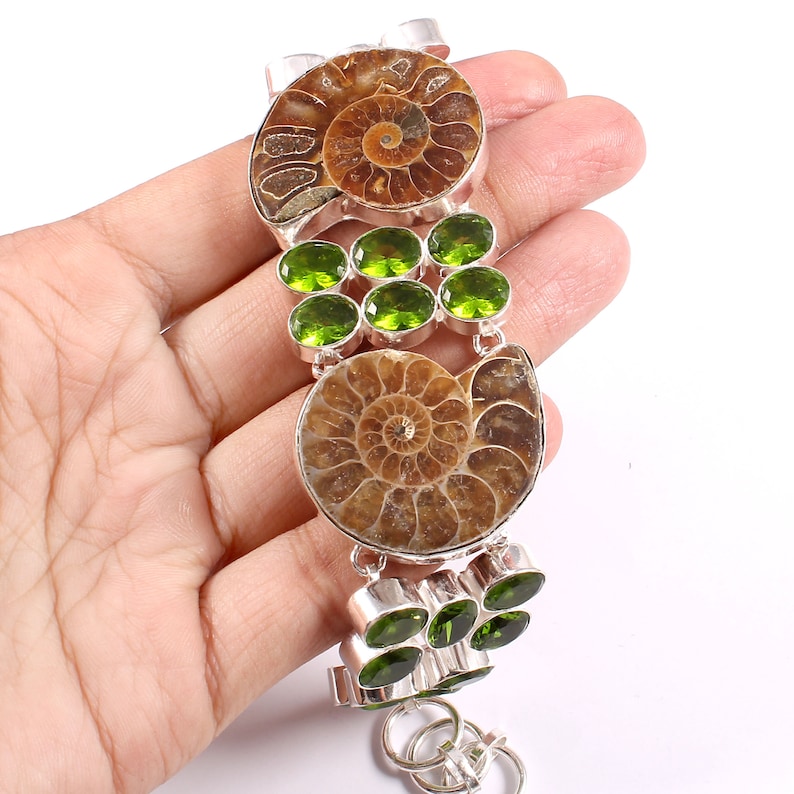 May include: A silver bracelet with two fossilized ammonites and green peridot gemstones. The bracelet has a lobster claw clasp.