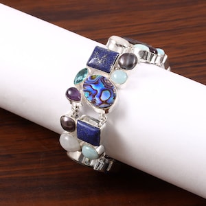 May include: A silver bracelet with a variety of colorful gemstones, including lapis lazuli, amethyst, abalone, and aquamarine.