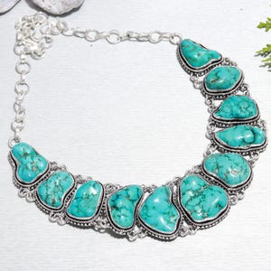 Könnte beinhalten: Eine türkisfarbene Halskette aus Silber mit einem geschwungenen Design. Die Halskette ist mit großen, unregelmäßigen Türkis-Steinen besetzt, die in Silber gefasst sind.