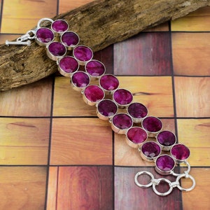 Könnte beinhalten: Ein silbernes Armband mit einer doppelten Reihe runder, rosafarbener Rubin-Edelsteine. Das Armband hat einen Karabinerverschluss und zwei Sprungringe.