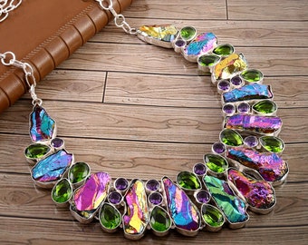 Puede incluir: Un collar de plata con piedras iridiscentes de colores arcoíris y detalles verdes y morados. El collar está hecho de plata y presenta una variedad de piedras de diferentes formas.