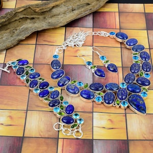 Puede incluir: Un collar y pendientes de plata con detalles de piedras preciosas azules y verdes. El collar tiene un colgante en forma de lágrima y los pendientes son de estilo gota.