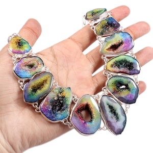 Puede incluir: Un collar de plata con un colgante de ágata iridiscente arcoíris. El colgante es una piedra grande de forma ovalada con un agujero en el centro. El collar está hecho de eslabones de cadena de plata.