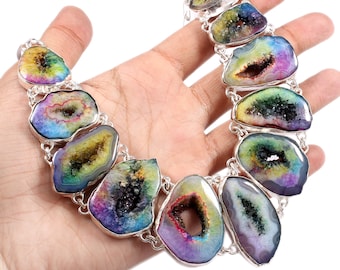Puede incluir: Un collar de plata con un colgante de ágata iridiscente arcoíris. El colgante es una piedra grande de forma ovalada con un agujero en el centro. El collar está hecho de eslabones de cadena de plata.