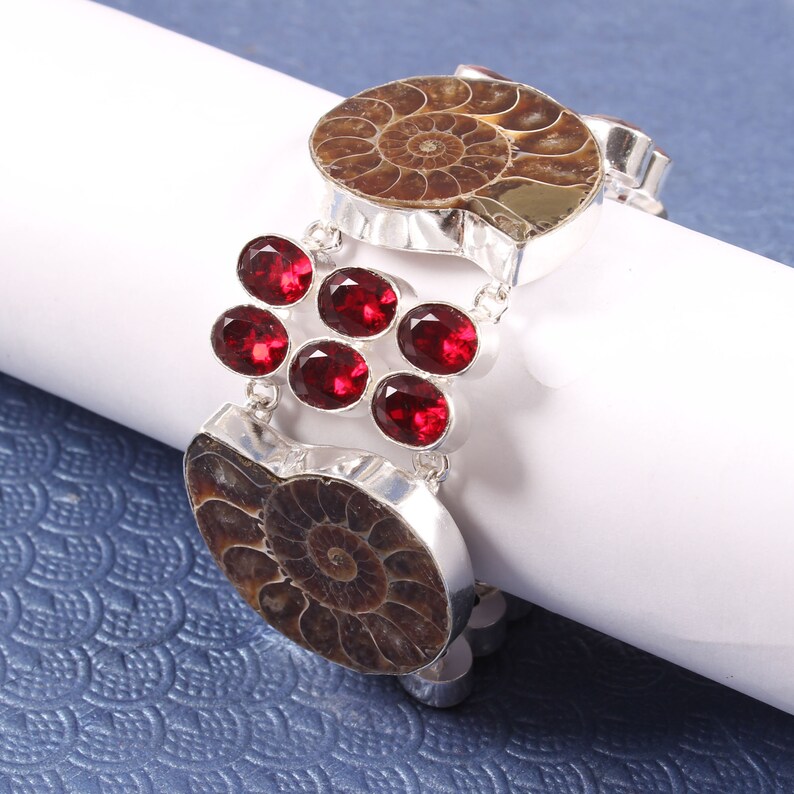 May include: A silver bracelet with two brown ammonite fossils and red gemstone accents.
