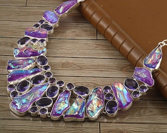Puede incluir: Un collar de plata con un gran colgante de cristal morado iridiscente y piedras de amatista más pequeñas. El collar está sobre una superficie de madera.