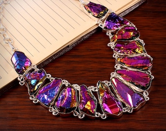 Puede incluir: Un collar de plata con una fila de colgantes de piedras preciosas iridiscentes de color púrpura y azul. El collar está sobre una superficie de madera.