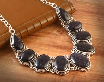 Puede incluir: Un collar de plata con un colgante en forma de lágrima y piedras ovaladas. Las piedras son de color azul oscuro con un acabado brillante.