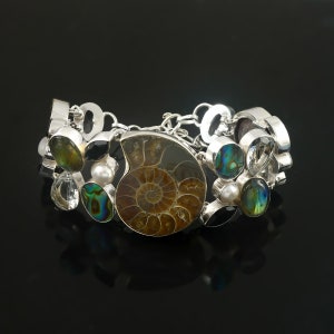 May include: A silver bracelet with a variety of gemstones, including a large ammonite fossil, abalone shell, and clear quartz crystals.