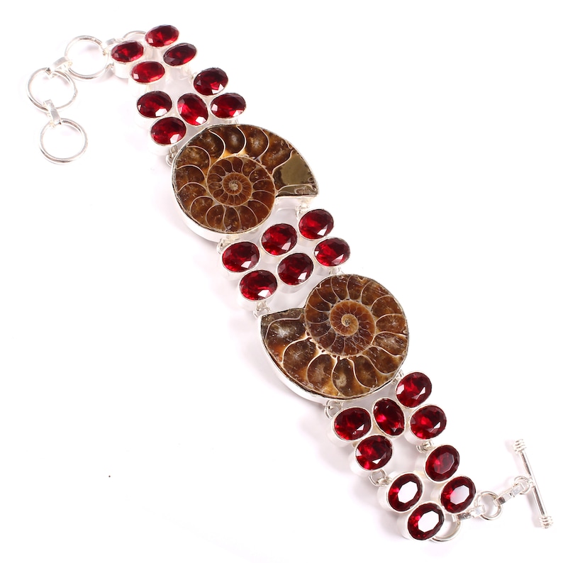 May include: A silver bracelet with two fossilized ammonites and red gemstones. The bracelet has a toggle clasp.