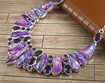 Puede incluir: Un collar de plata con un gran colgante de cristal morado. El colgante está hecho de muchos cristales más pequeños que son iridiscentes y tienen un efecto arcoíris. El collar está sobre una superficie de madera.