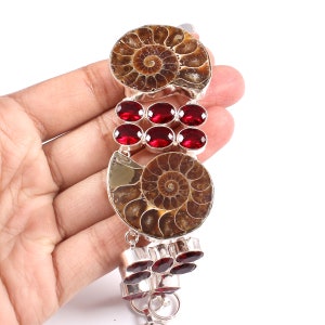 May include: A silver bracelet with two fossilized ammonite shells and red gemstone accents.