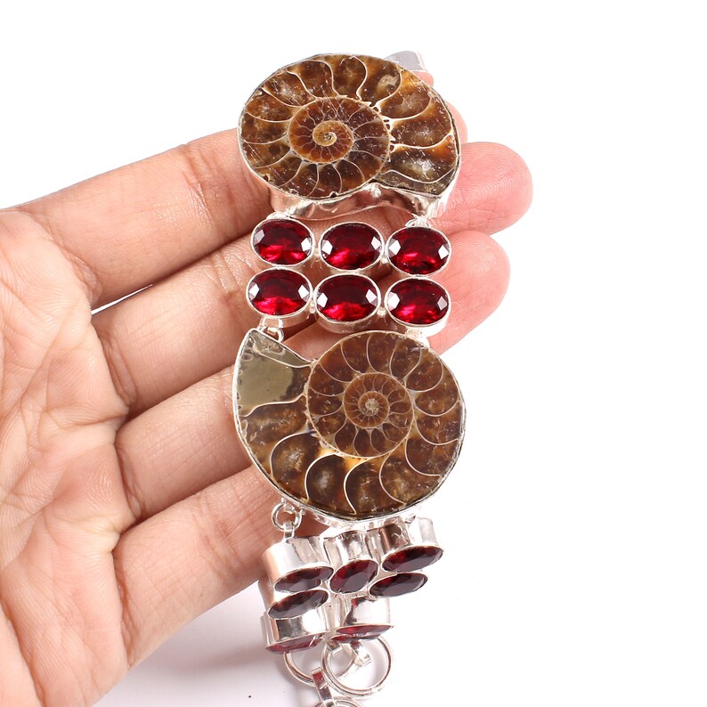 May include: A silver bracelet with two fossilized ammonite shells and red gemstone accents.