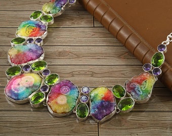 Puede incluir: Un collar de cristal arcoíris con detalles plateados. El collar presenta una variedad de cristales coloridos, incluyendo amatista y piedras verdes.