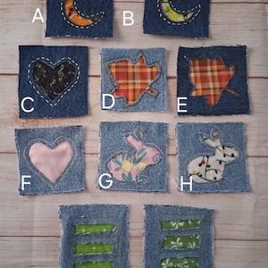 May include: A collection of ten denim patches with various appliqued designs. The patches feature a crescent moon, heart, leaf, and rabbit motifs. Some patches have green or patterned fabric inserts. The patches are square and have a raw edge.