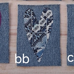 May include: Three denim fabric squares with heart cutouts. The hearts are filled with different patterned fabrics: a purple batik, a blue and white floral, and a teal floral. Each square has a white letter designation.