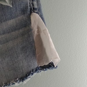 May include: A pair of light blue denim shorts with a white lace trim on the bottom hem. The shorts have a floral design on the front.