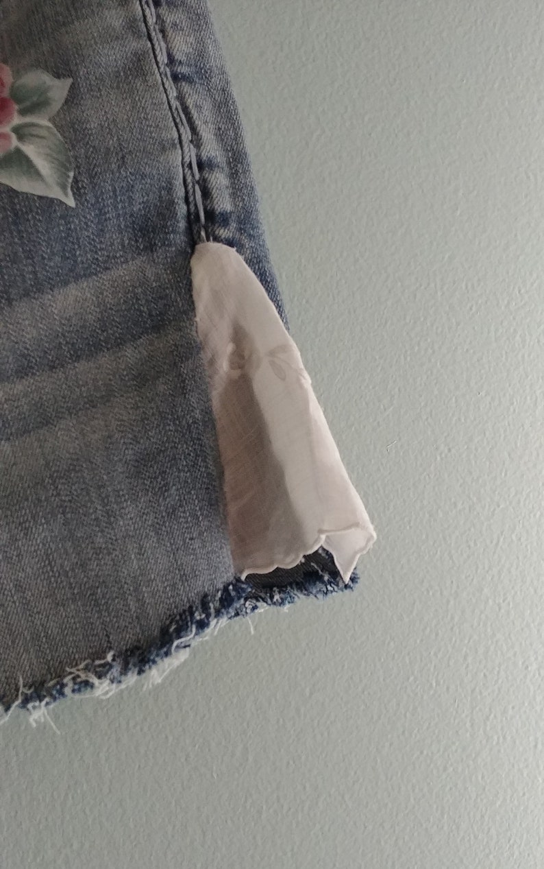 May include: A pair of light blue denim shorts with a white lace trim on the bottom hem. The shorts have a floral design on the front.