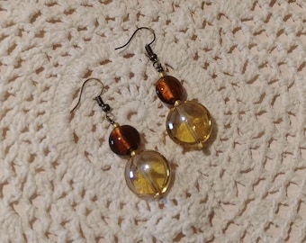 May include: A pair of dangle earrings with two amber glass beads on each earring. The top bead is a darker amber color and the bottom bead is a lighter amber color. The earrings have a bronze-colored hook.