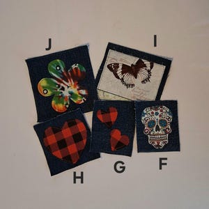 Puede incluir: Cinco parches de mezclilla con varios dise&ntilde;os. Un parche presenta una flor colorida, otro una mariposa y un tercero una calavera de az&uacute;car. Los parches restantes muestran corazones, incluido un coraz&oacute;n a cuadros rojo y negro.