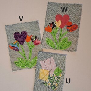 Puede incluir: Tres parches de tela vaquera con dise&ntilde;os de corazones florales. Cada parche tiene una letra diferente: V, W y U. Los corazones son de varios colores y patrones, con tallos y hojas verdes. Los parches est&aacute;n sobre un fondo blanco.