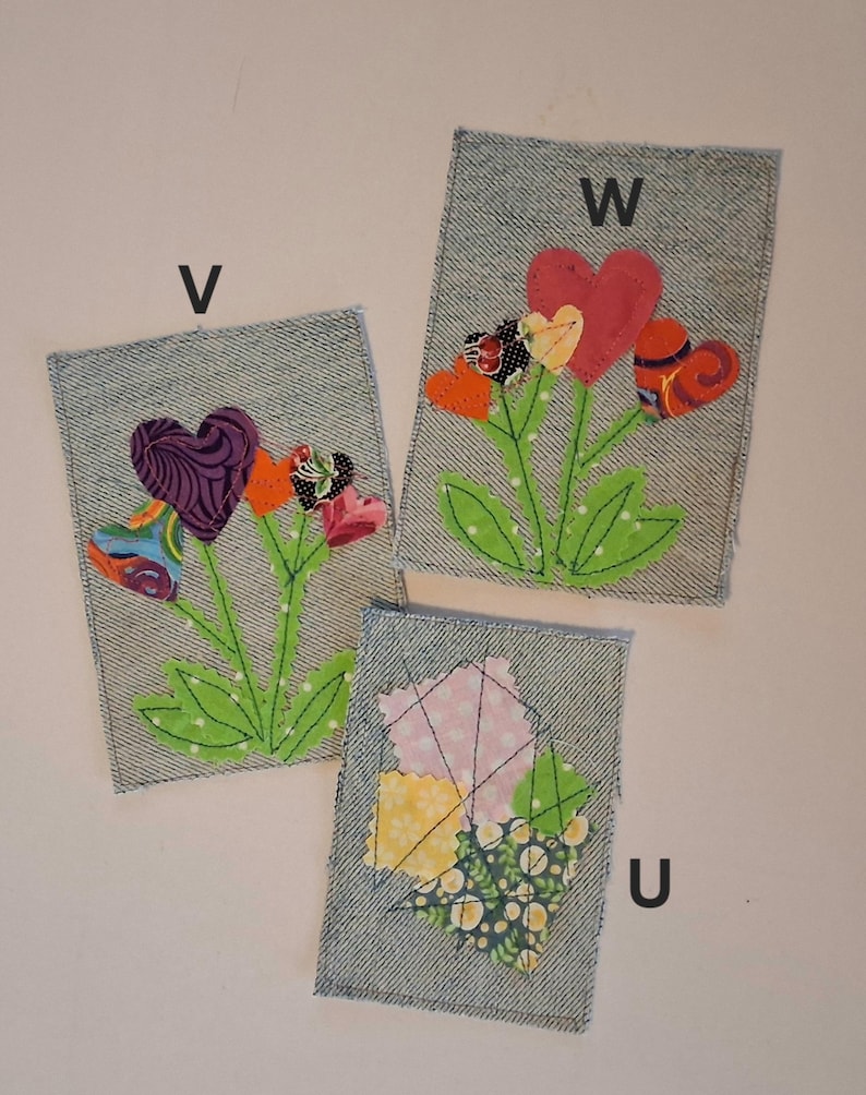 Puede incluir: Tres parches de tela vaquera con dise&ntilde;os de corazones florales. Cada parche tiene una letra diferente: V, W y U. Los corazones son de varios colores y patrones, con tallos y hojas verdes. Los parches est&aacute;n sobre un fondo blanco.