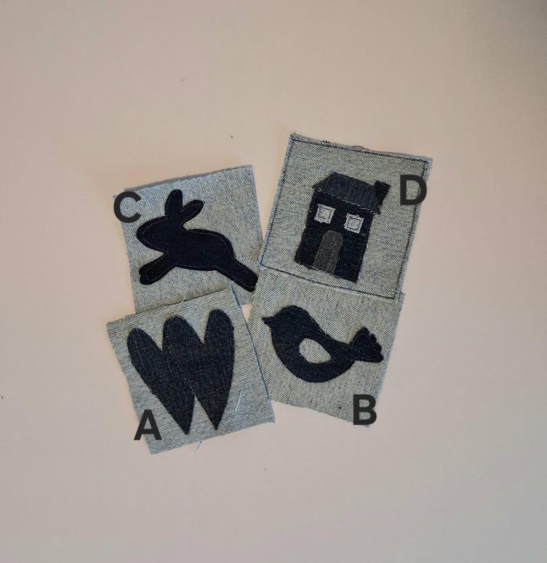 Puede incluir: Cuatro cuadrados de tela vaquera con dise&ntilde;os aplicados en negro: una letra "W", un p&aacute;jaro, un conejo y una casa. Los cuadrados est&aacute;n dispuestos sobre una superficie rosa claro. Los dise&ntilde;os est&aacute;n cosidos sobre la tela vaquera.
